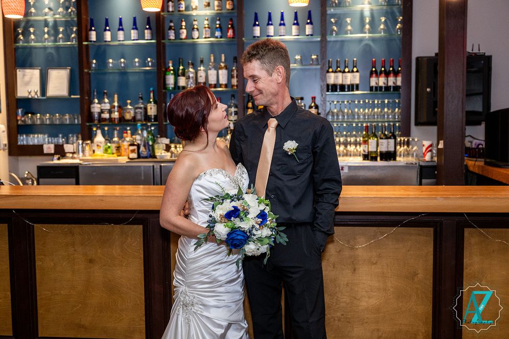 Couple shares intimate moment at modern bar with blue-lit bottle display wall.