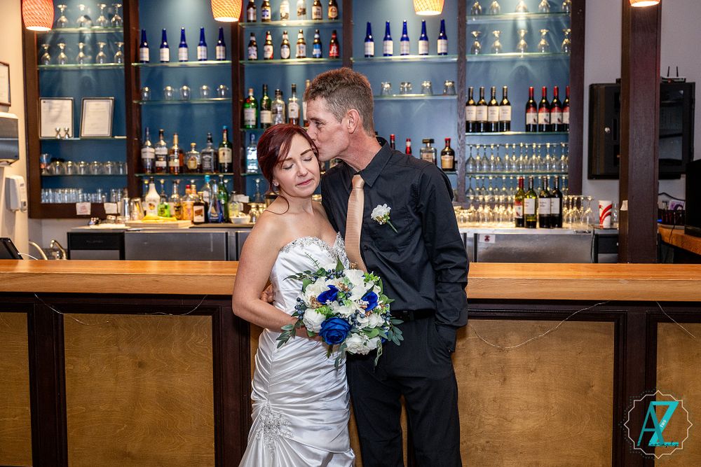 Romantic moment captured at upscale bar with illuminated shelving and pendant lights.