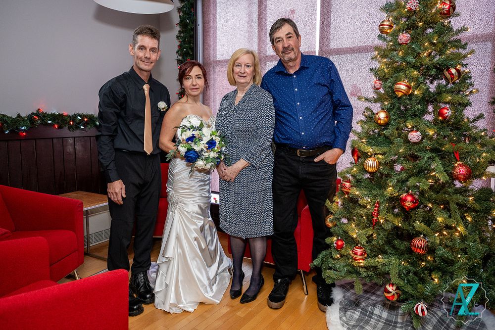Wedding group poses by decorated Christmas tree in room with red couch.
