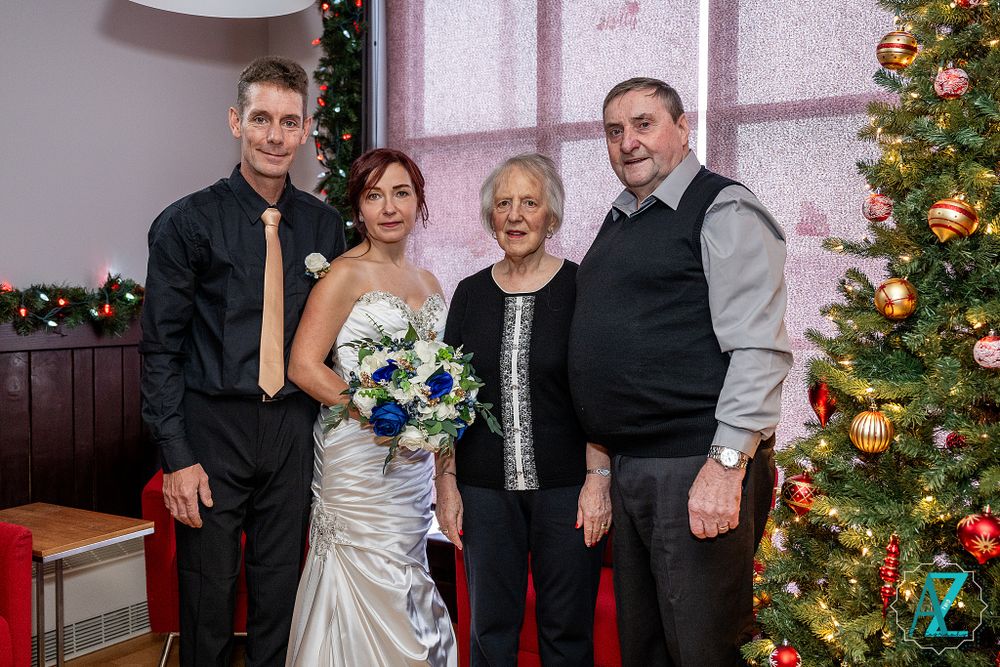 Family portrait by Christmas tree with decorated presents and red furniture.