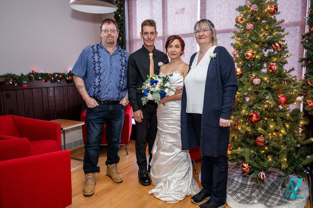 Wedding party poses in front of decorated Christmas tree with red couch and festive holiday decor.