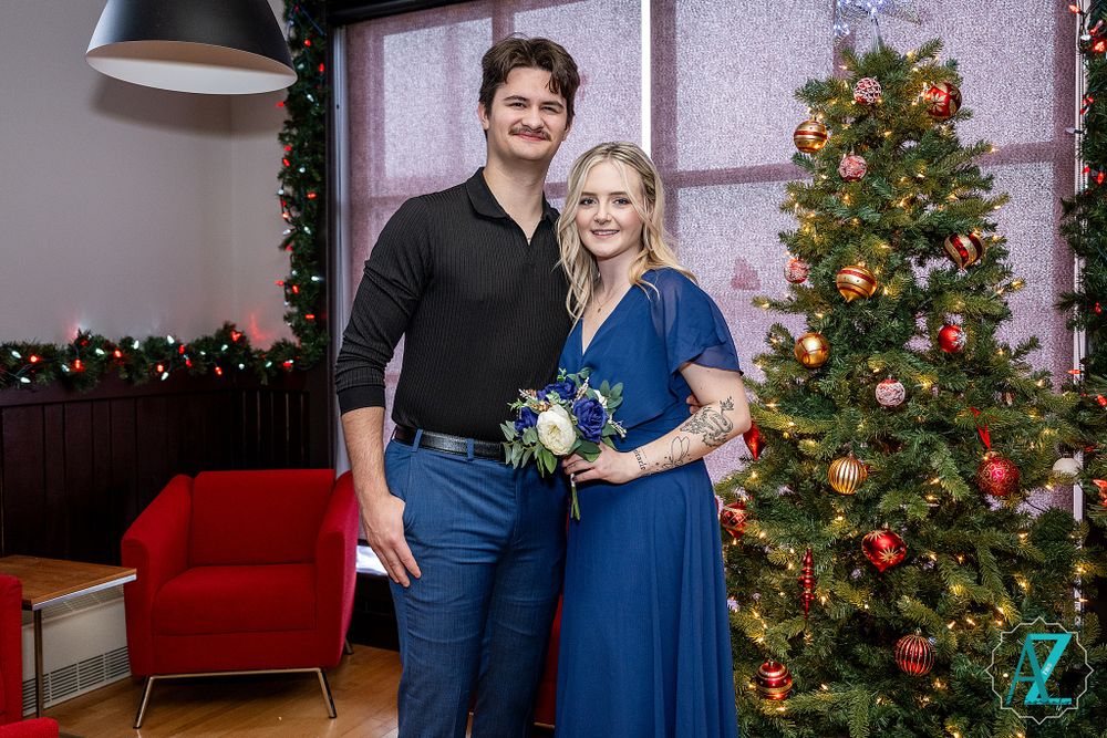 Couple poses by decorated Christmas tree and red couch during holiday celebration.