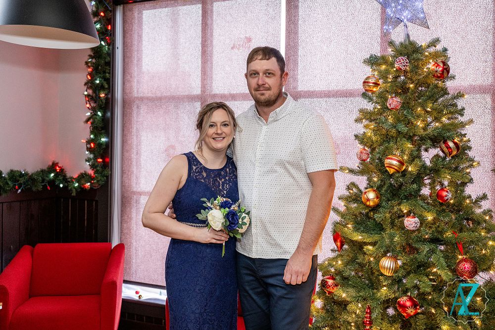 Couple poses together by decorated Christmas tree during holiday celebration.