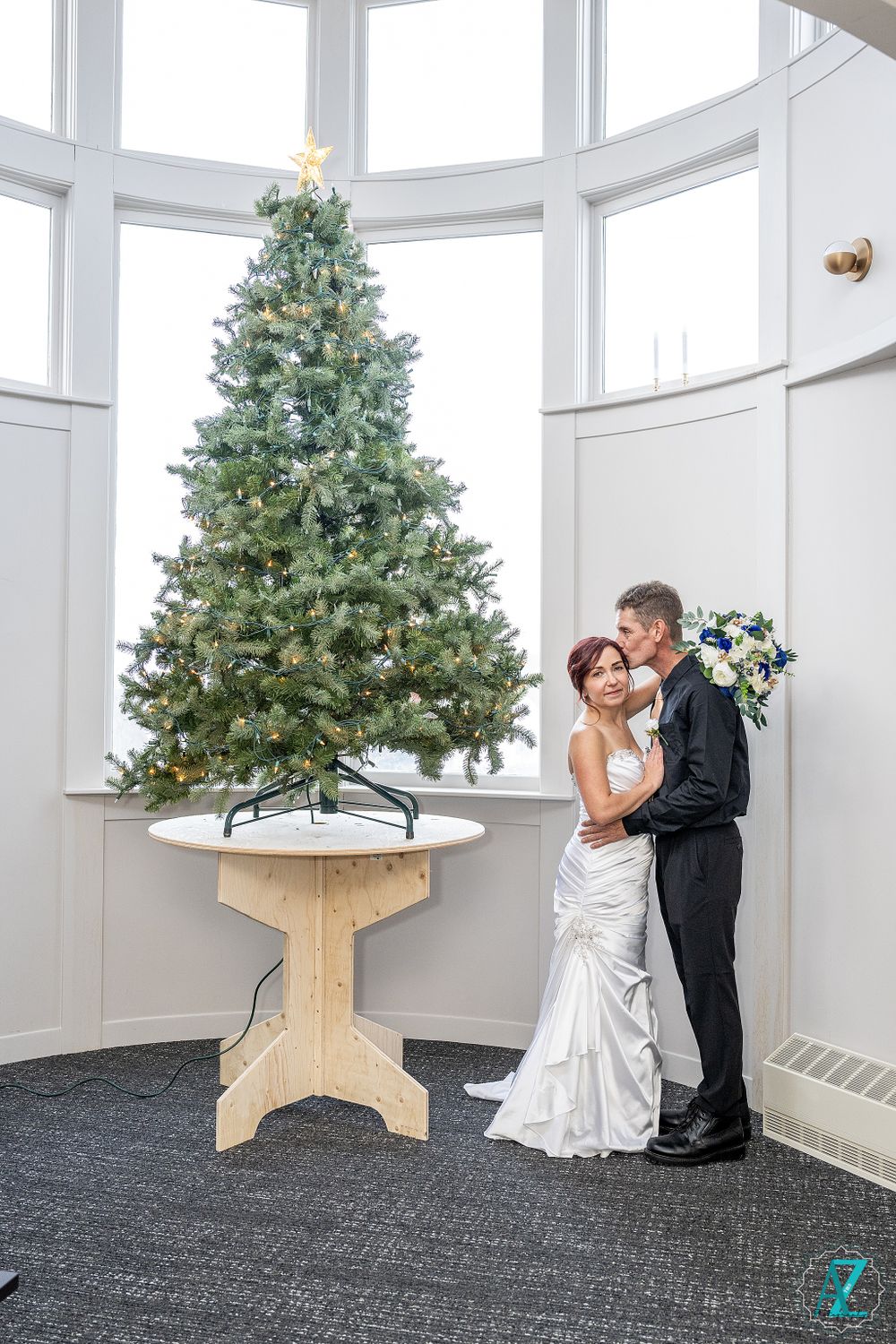 Elegant holiday wedding scene with couple embracing by lit Christmas tree.