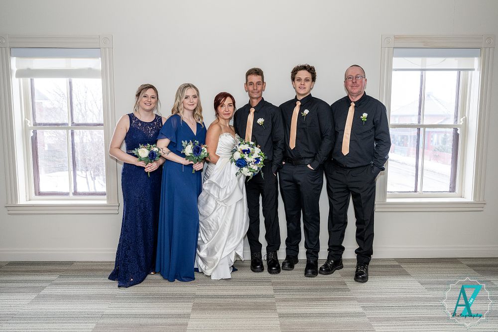 Wedding party poses in a bright white room wearing navy blue and black formal attire.