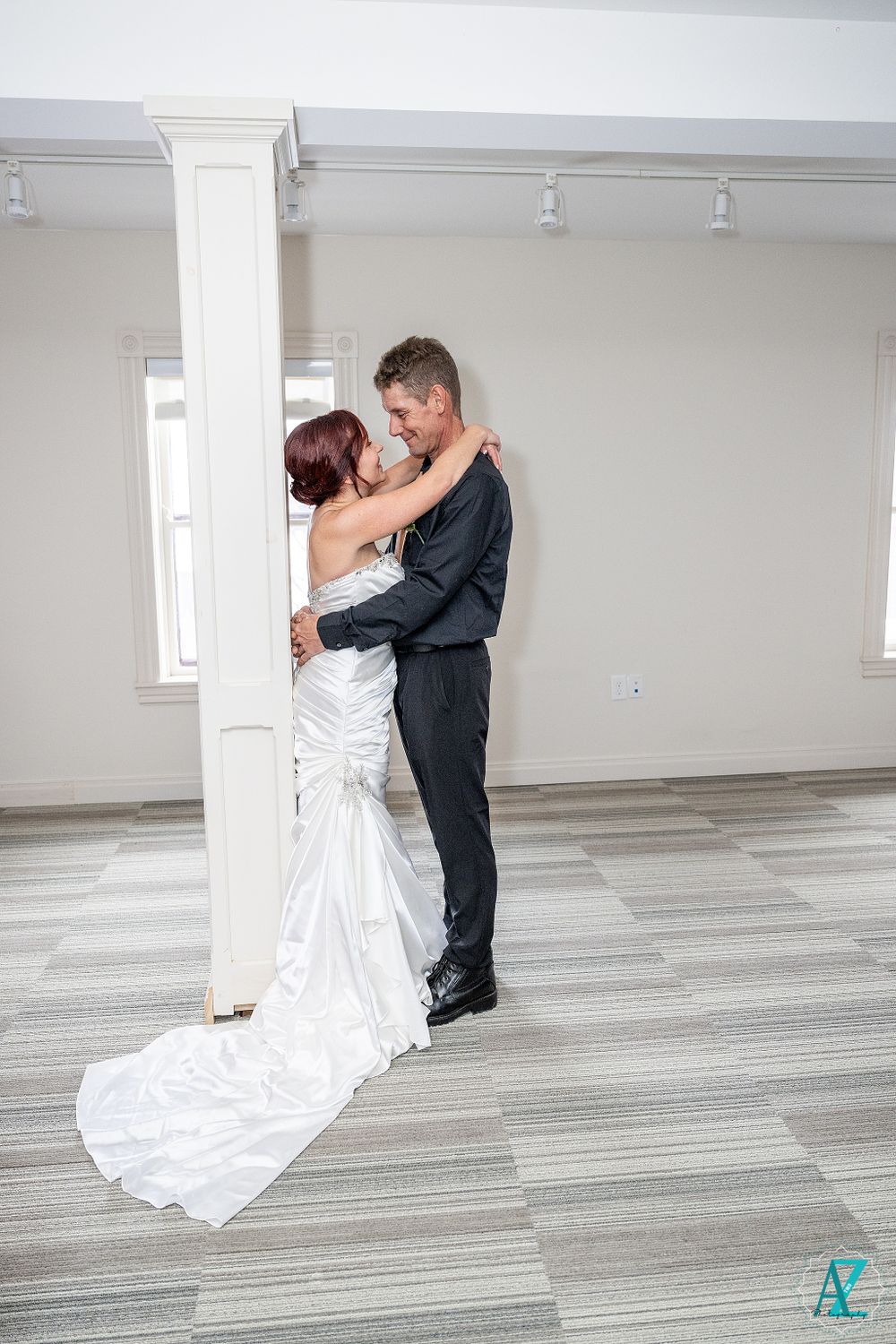 Wedding couple shares romantic moment by white pillar with long train of dress visible.