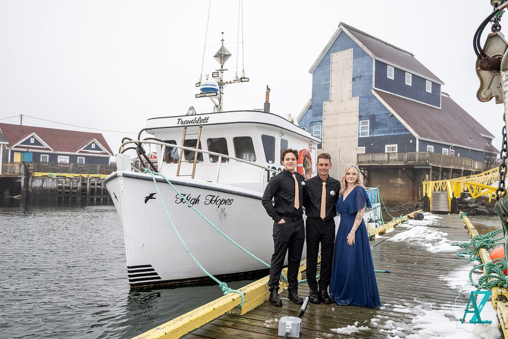 Wedding group poses on dock next to large white fishing boat named 'High Hope'.