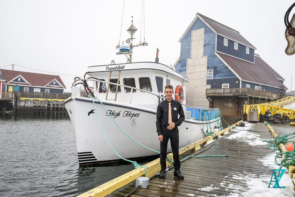 Formal dressed couple stands on snowy dock beside white fishing vessel.