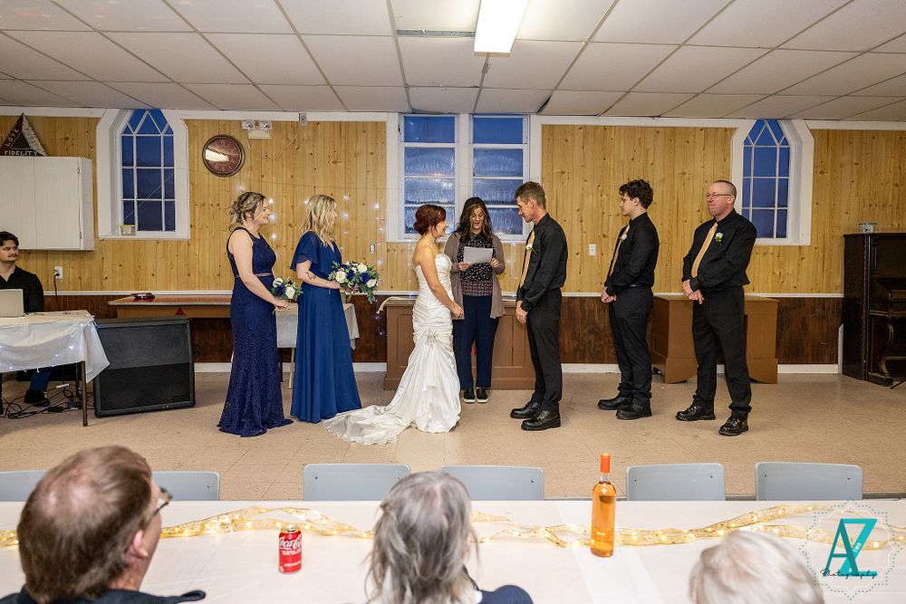 Wedding ceremony in progress with attendants in blue dresses and formal attire on a raised platform.