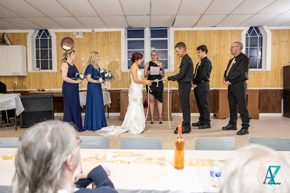 Wedding ceremony with attendants gathered on stage in a community hall setting.