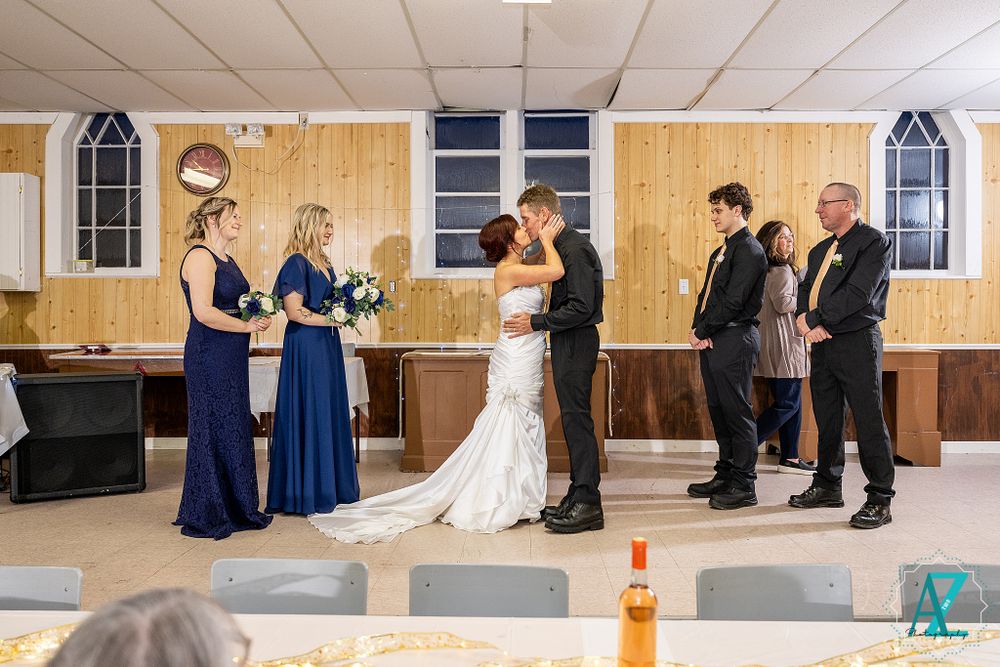 Wedding ceremony moment with attendants in navy blue dresses and formal attire in a community hall.