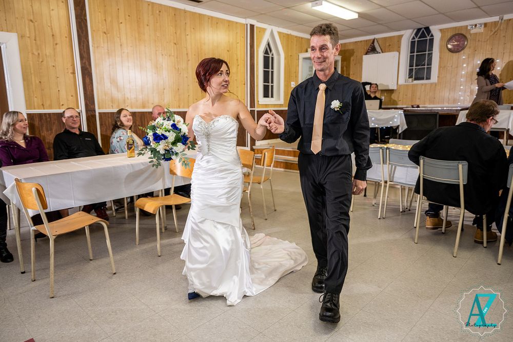 Elegant couple dances together in a church reception hall with wooden walls and white tables.