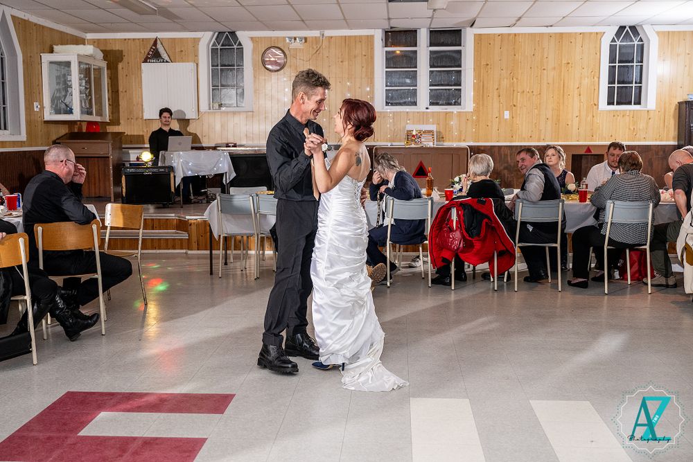 Romantic dance on a checkered floor in a church hall with guests watching from tables.