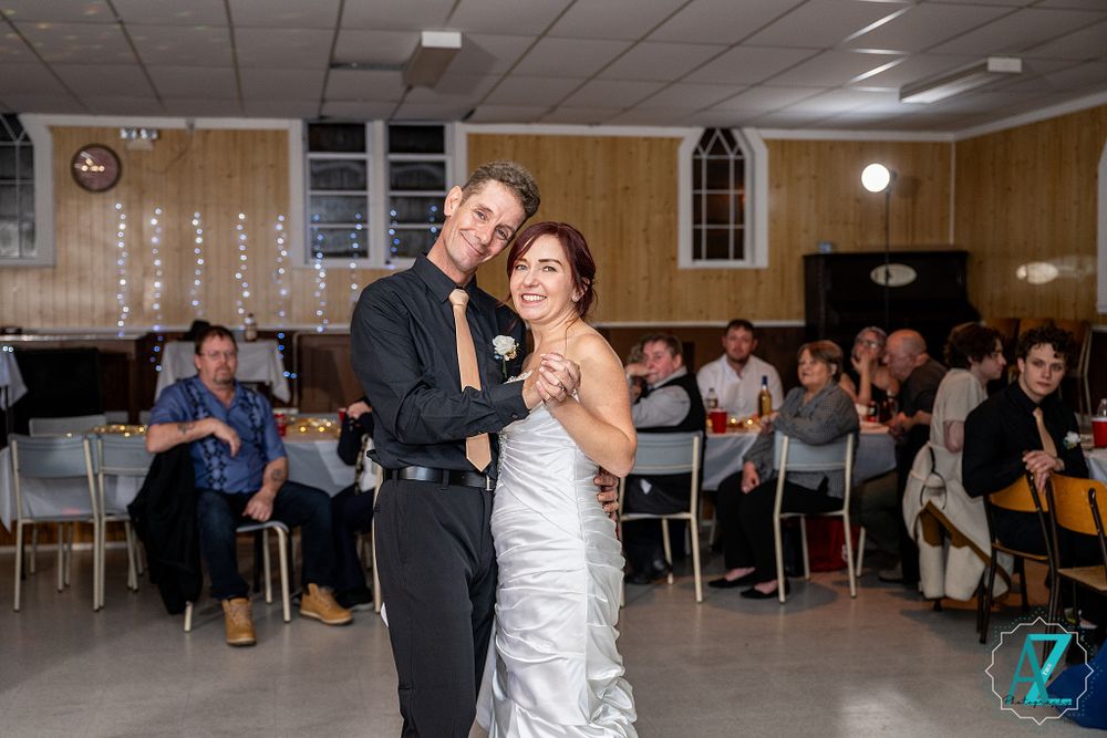 Dancing couple shares a tender moment in a church hall with guests watching.