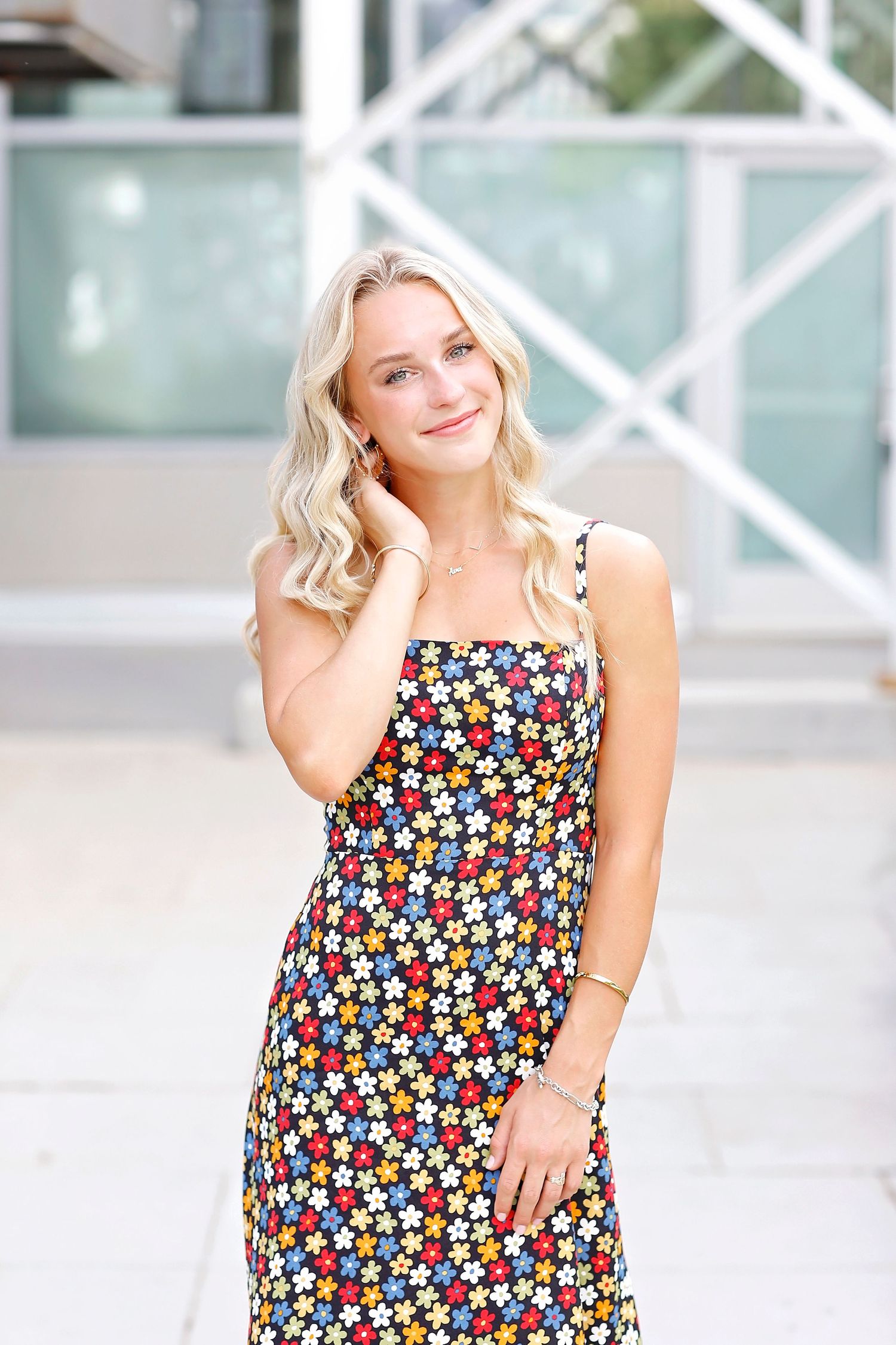 A portrait in a floral summer dress against modern architecture with glass panels.