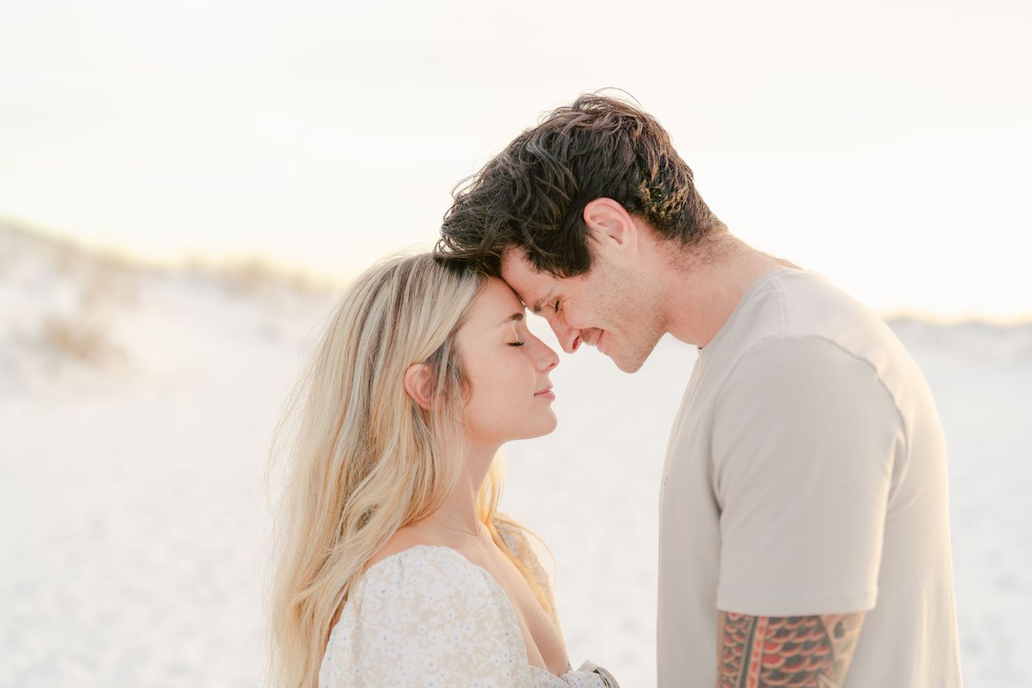 Intimate moment between couple on white sand beach at sunset.