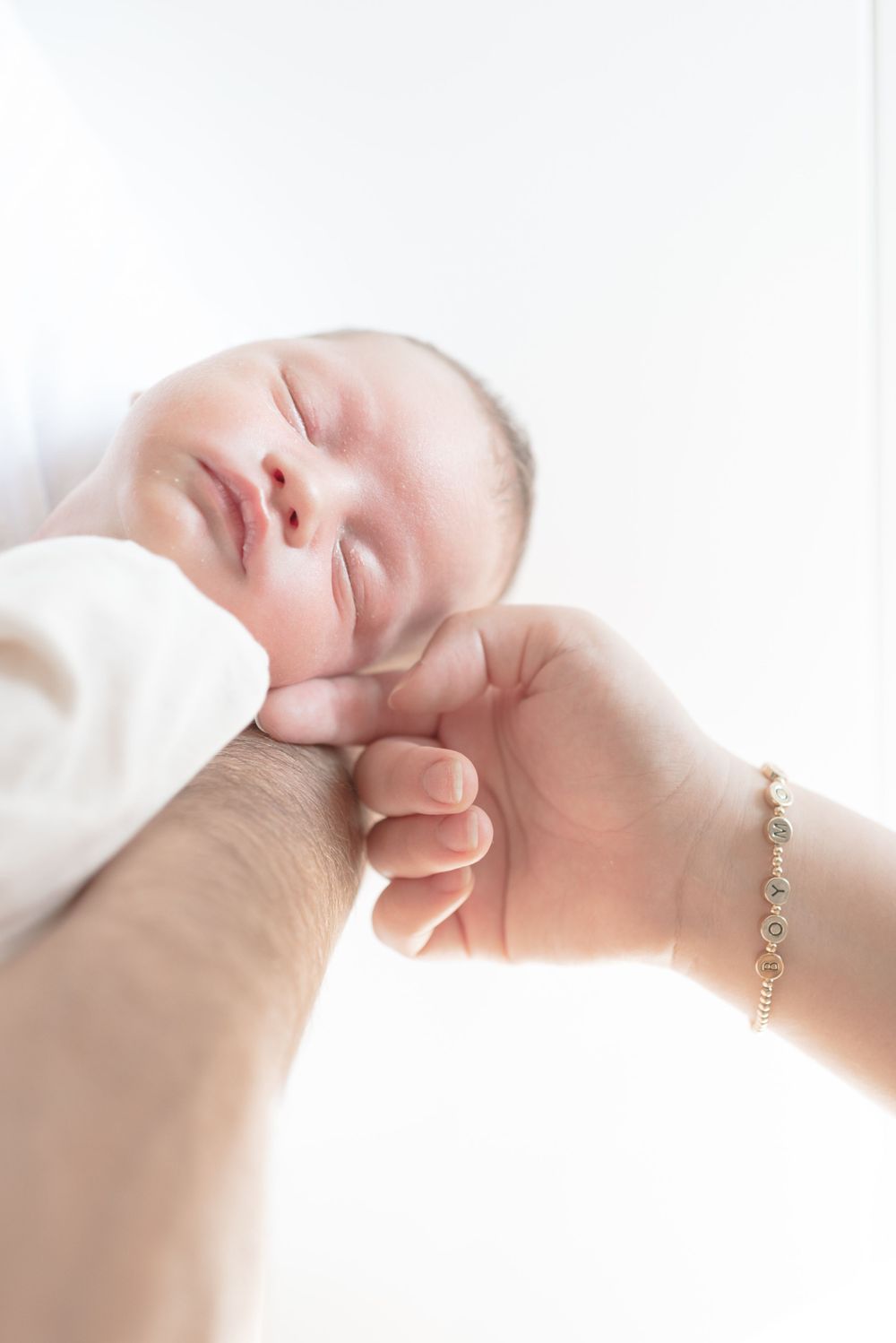 Newborn baby boy held in his father’s arms while mother gently caresses him during a lifestyle photoshoot in their Toronto home