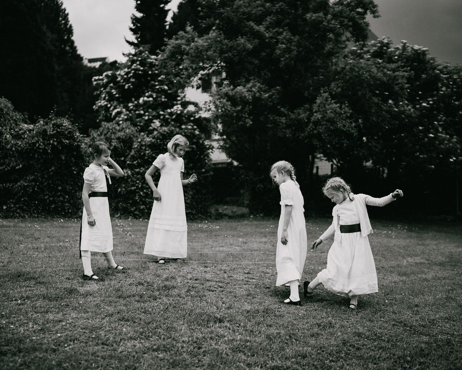 Vintage photograph of four women in white dresses playing or dancing in a garden.