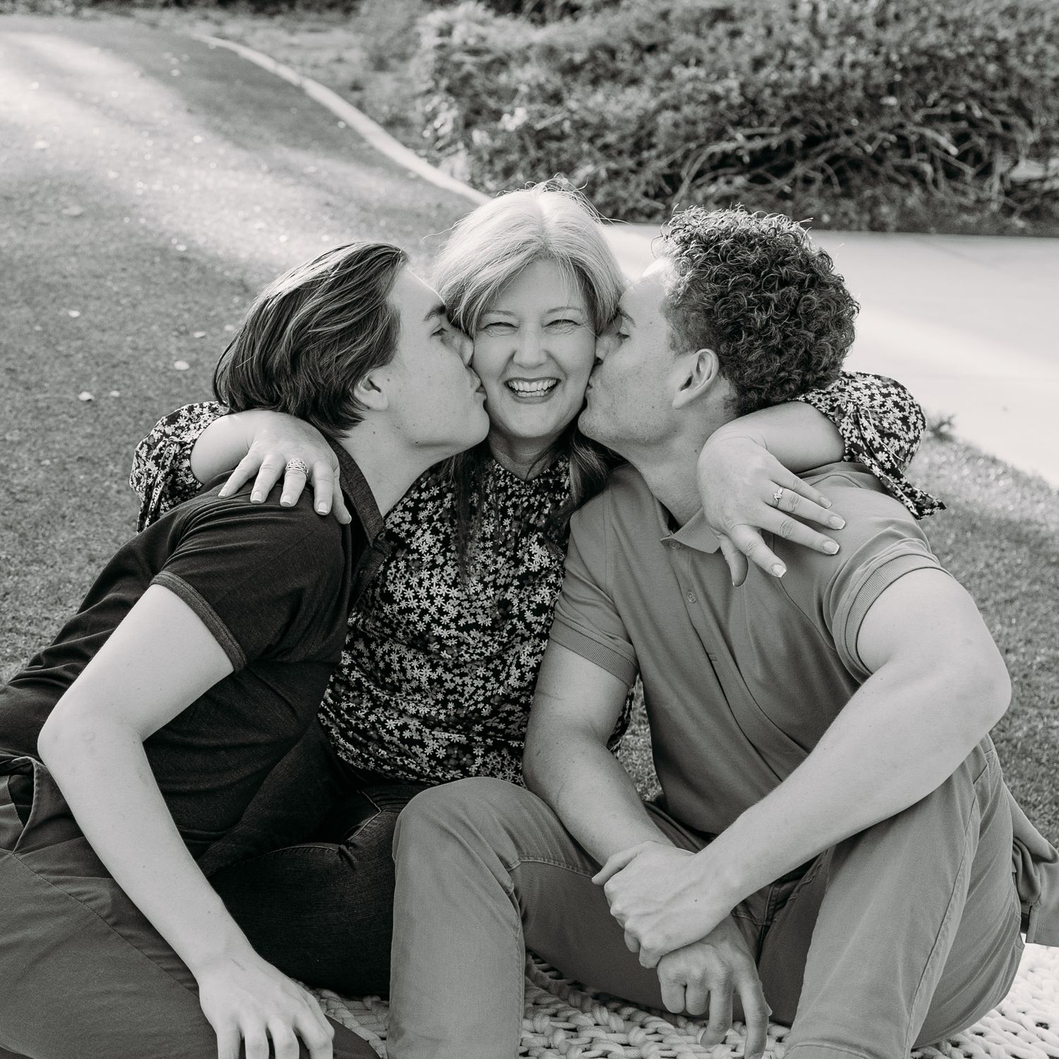 Two sons enthusiastically kissing their mom on each cheek.