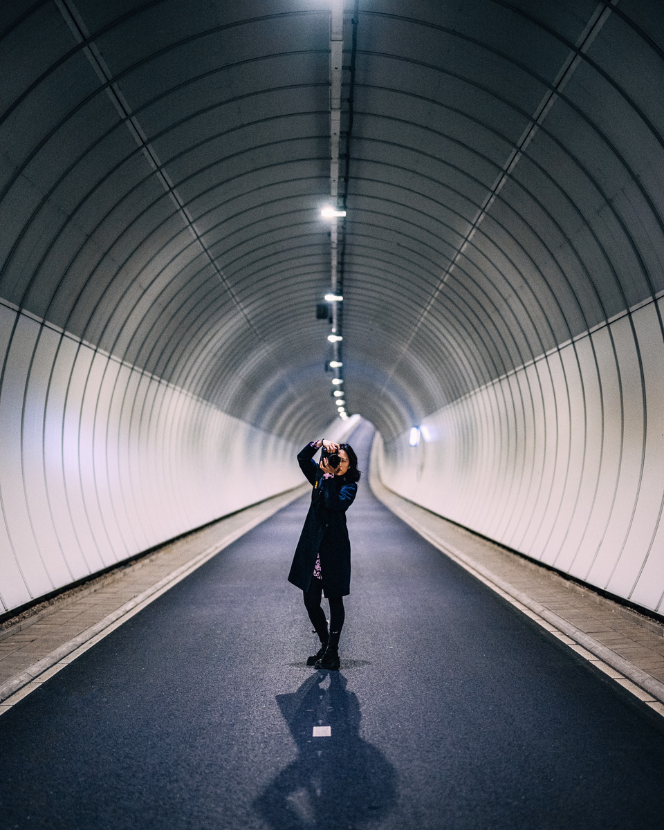 Silhouetted person in long tunnel with symmetrical lighting and curved architecture.