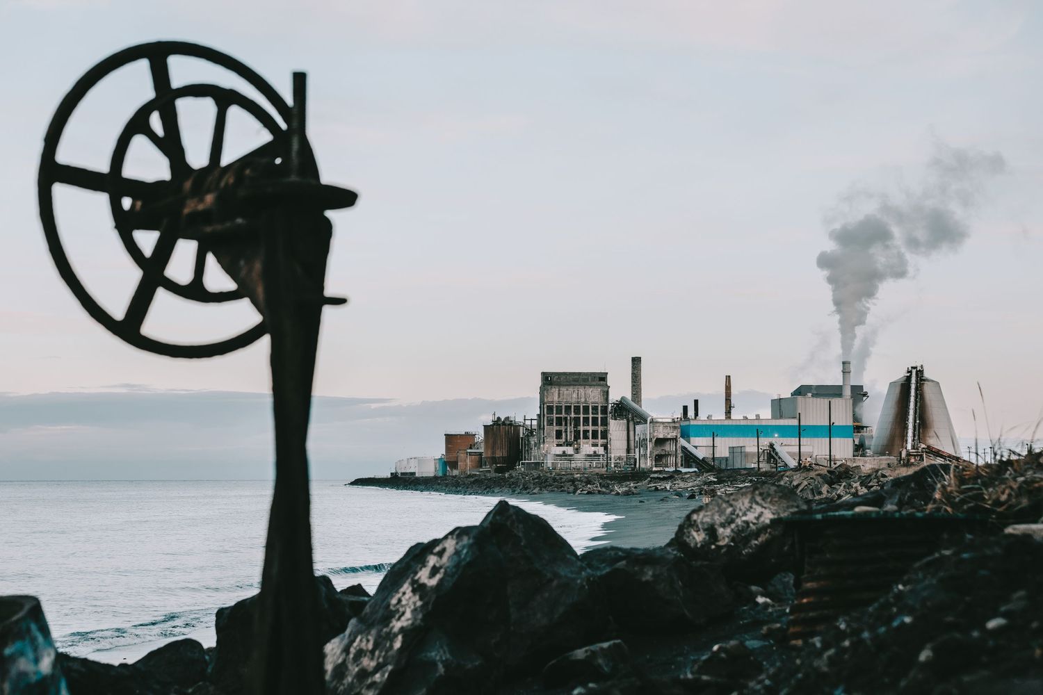 An industrial plant blowing smoke in the background of a beach.