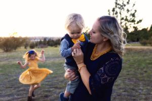 Two people in blue outfits share a moment outdoors while a child in a yellow dress dances in the background.