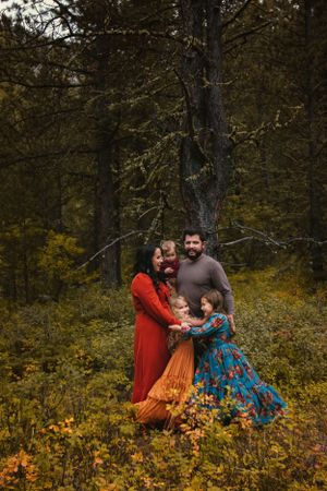 A  family embraces outdoors in autumn, wearing vibrant dresses in red, orange and blue among fall foliage in a forest setting.