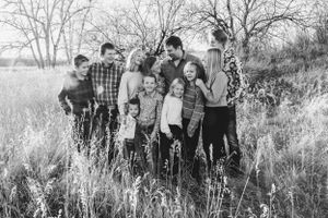 A large family poses together in a field of tall grass during autumn as bare trees stand in the background.