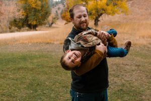 A playful moment captured outdoors against autumn trees showing spirited interaction on a grassy field.