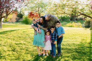 A family enjoys a sunny spring day together on a grassy lawn with blooming trees in the background.