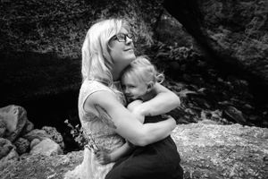 A black and white outdoor photo showing an embrace between two figures on a rocky outcrop in nature.