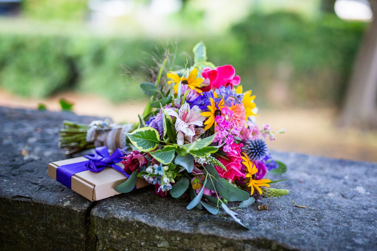 Colorful wedding flowers arranged on a stone wall outdoors.