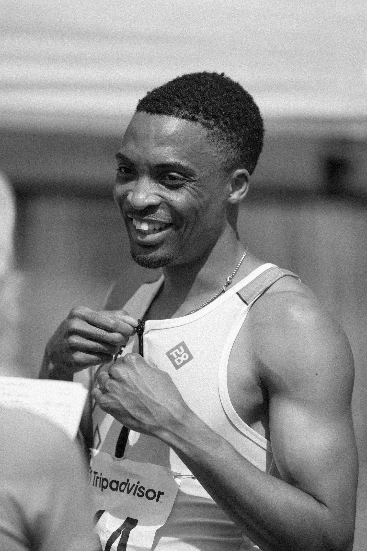 Track athlete in white singlet smiling during outdoor competition.