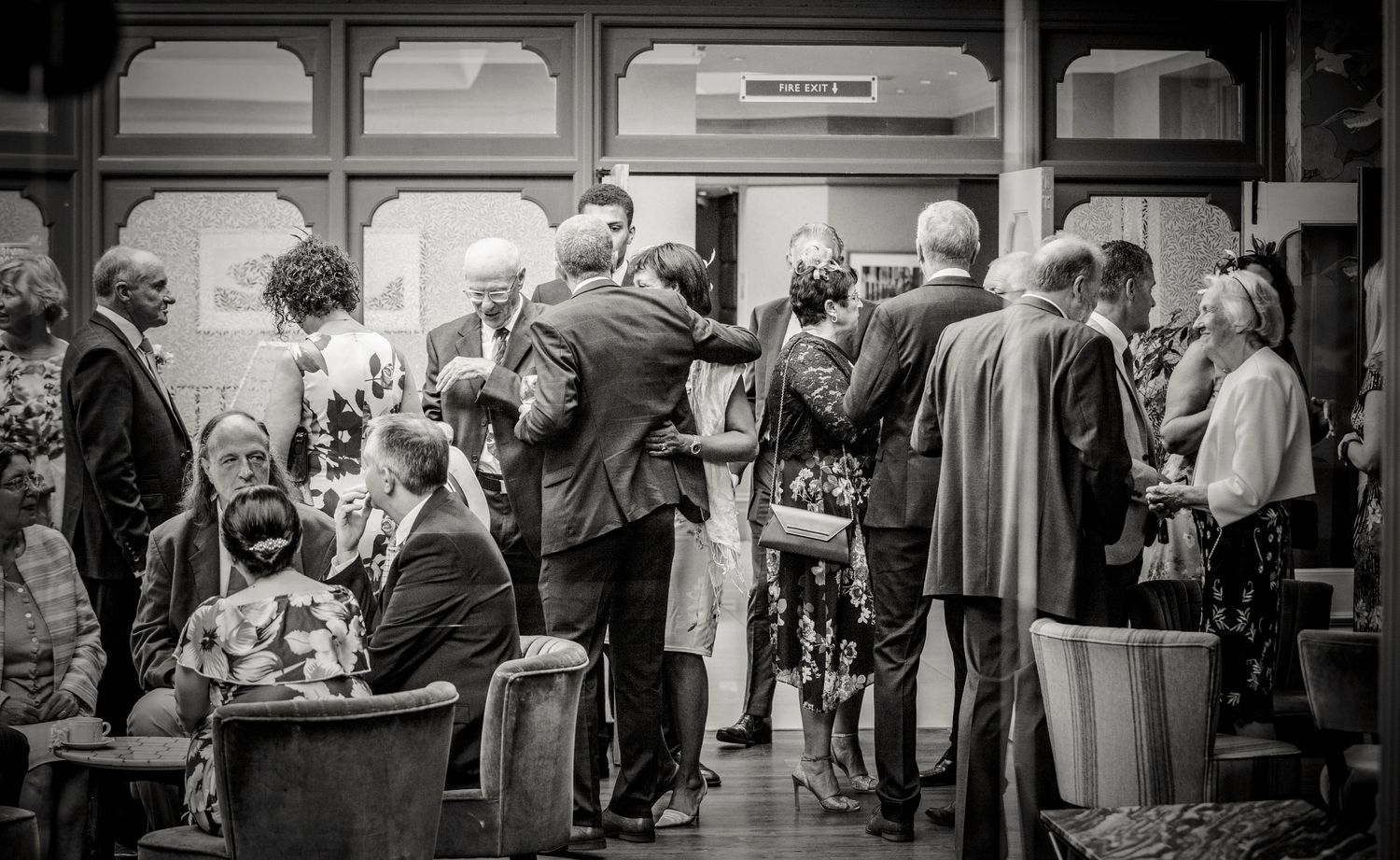Black and white photo of wedding guests mingling at indoor reception.