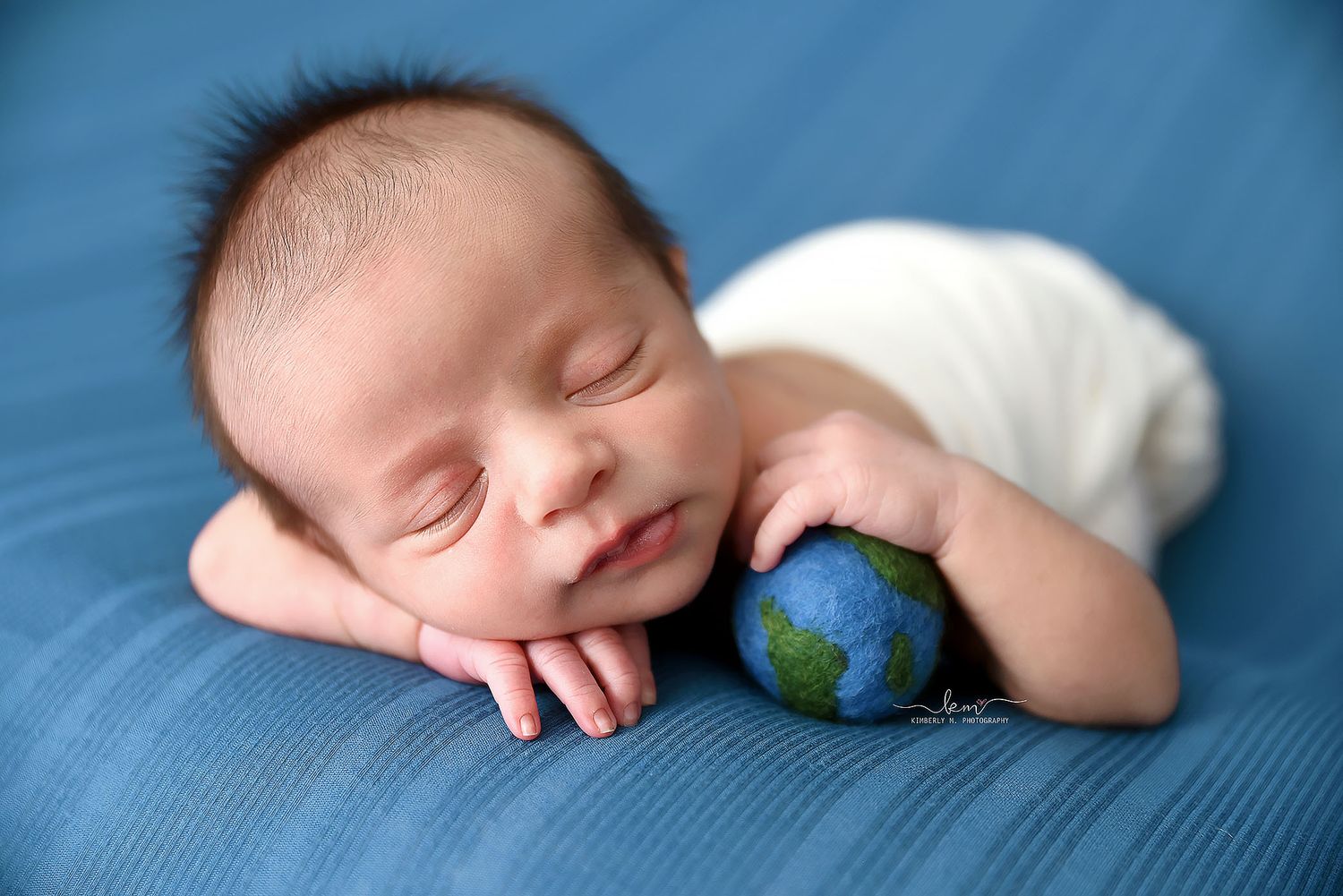 Peaceful newborn baby sleeping while holding a small globe on a blue background.