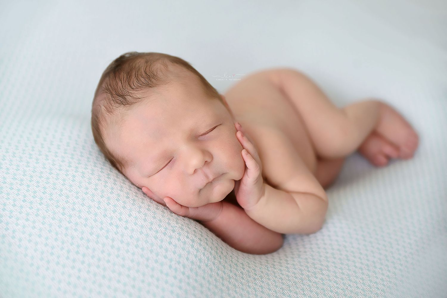 Peaceful sleeping newborn baby posed on a soft white textured blanket in a classic curled position.