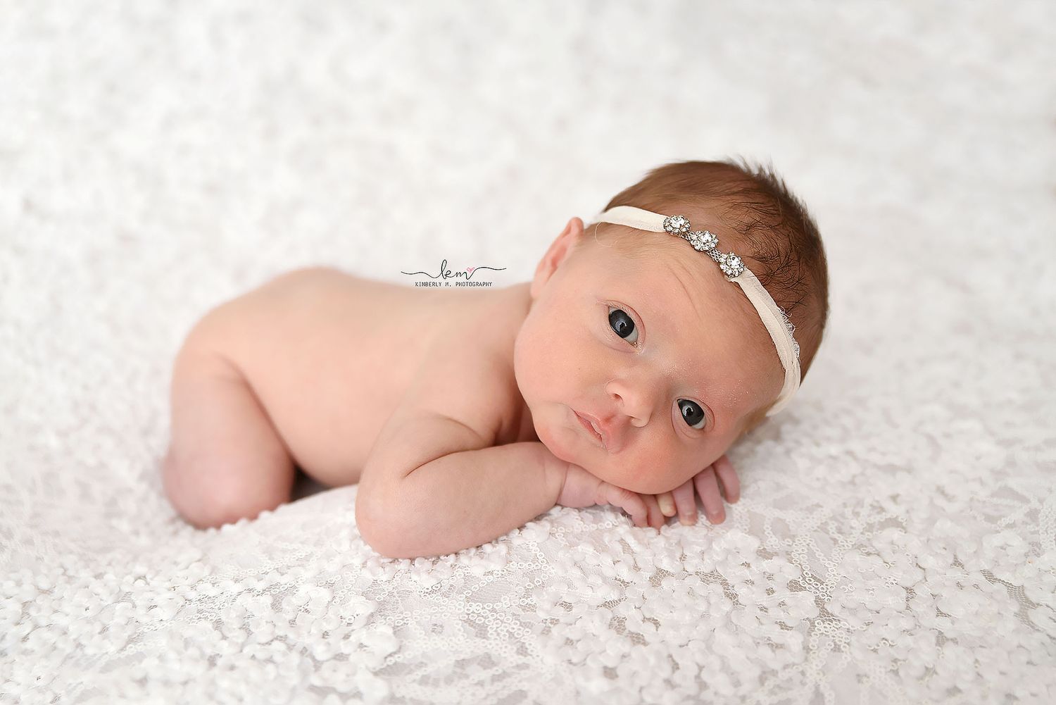 Alert newborn baby girl with blue eyes wearing a white headband on lace.