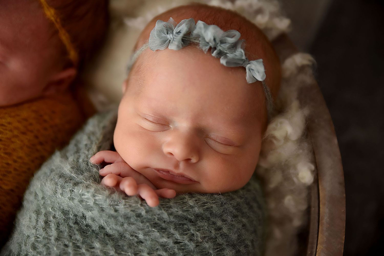 Sleeping newborn baby wrapped in teal with a matching floral headband in basket.