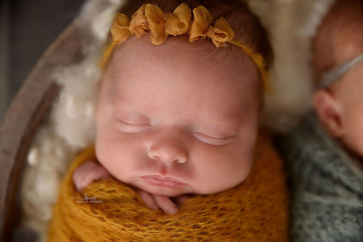 Close-up of a sleeping newborn baby wrapped in a mustard yellow knit swaddle with a matching floral headband.