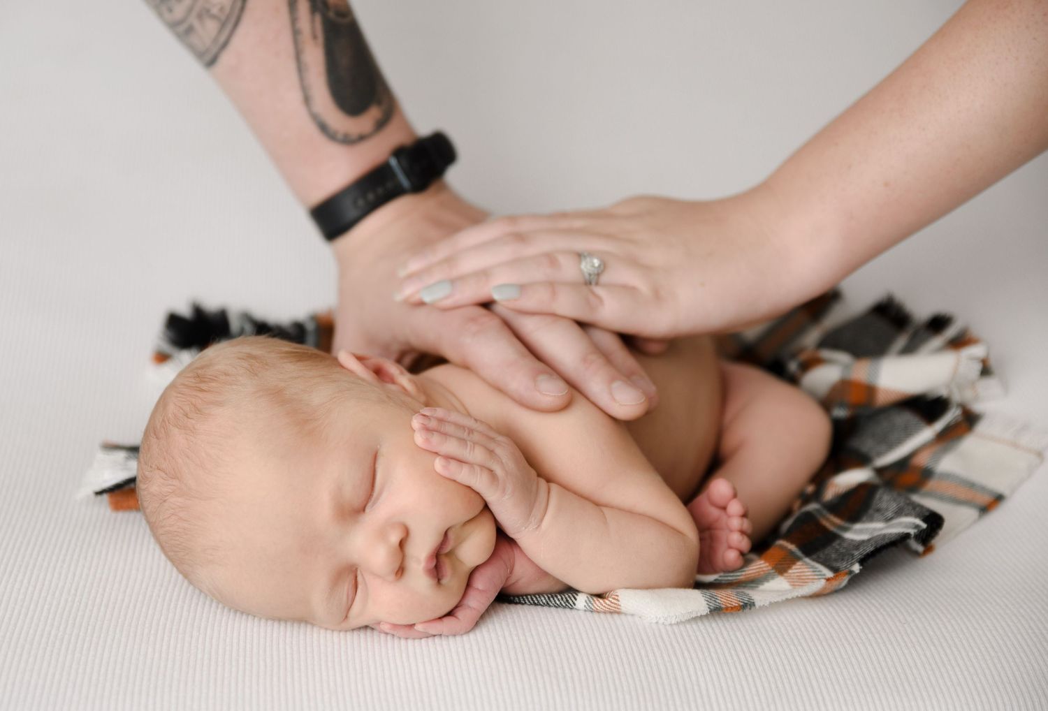 Newborn baby sleeping peacefully while parents gently place hands on infant during professional newborn photography session.