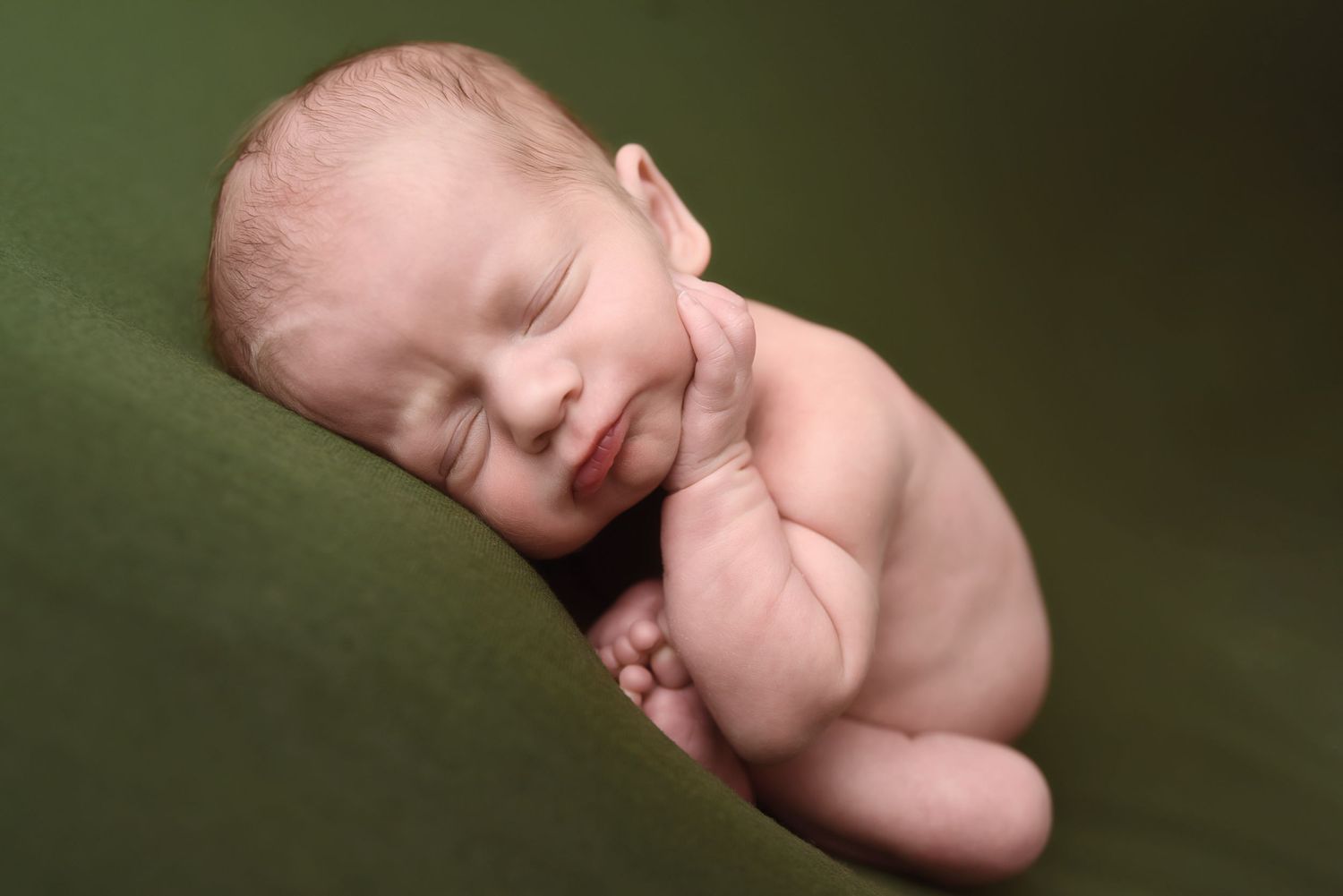 Peaceful sleeping newborn baby curled up on a soft green fabric background.