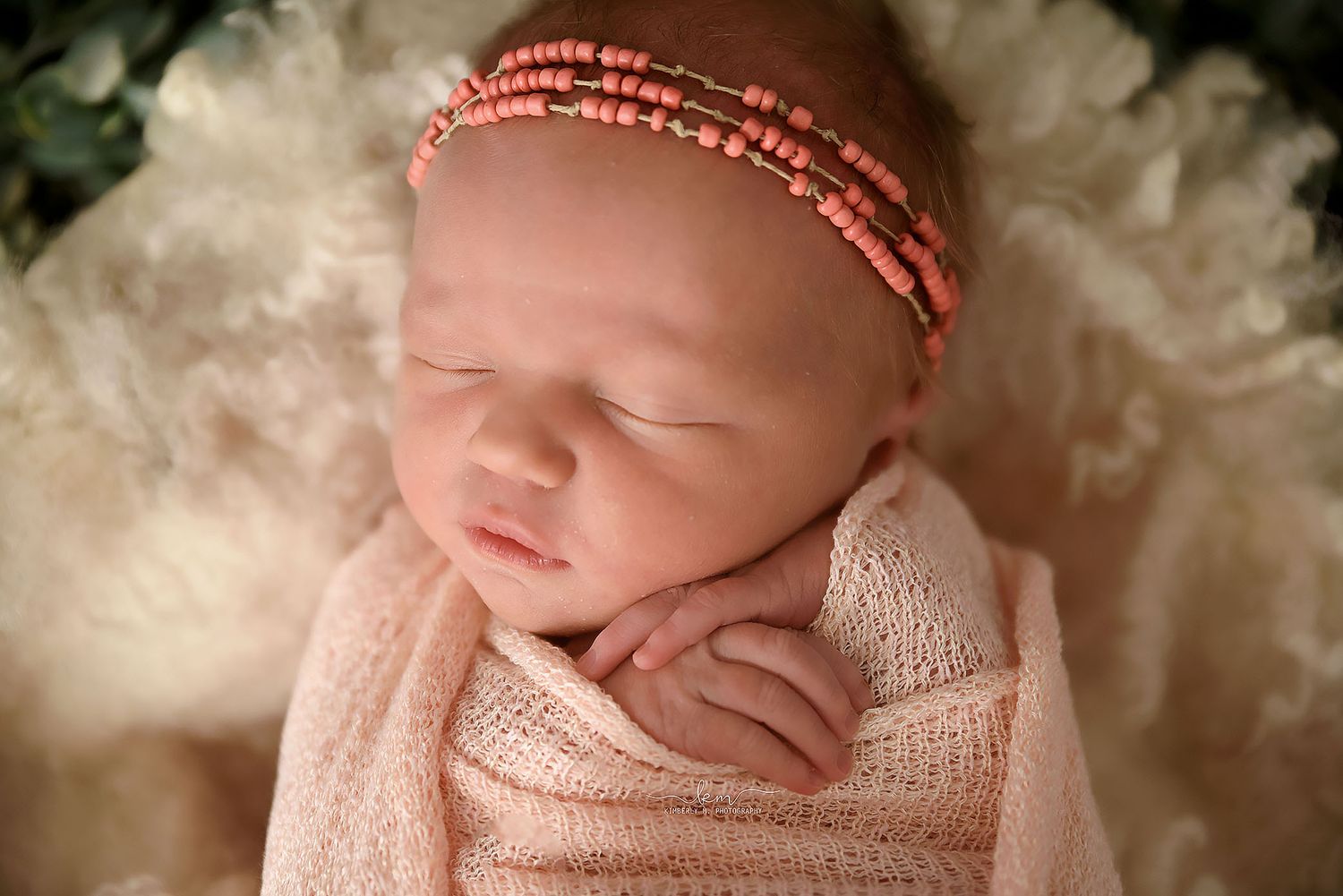 Sleeping newborn girl wrapped in pink with a delicate beaded coral headband.