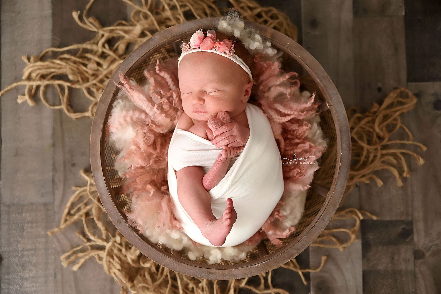 Newborn baby sleeping in a wooden bowl with pink ruffles and a floral crown.