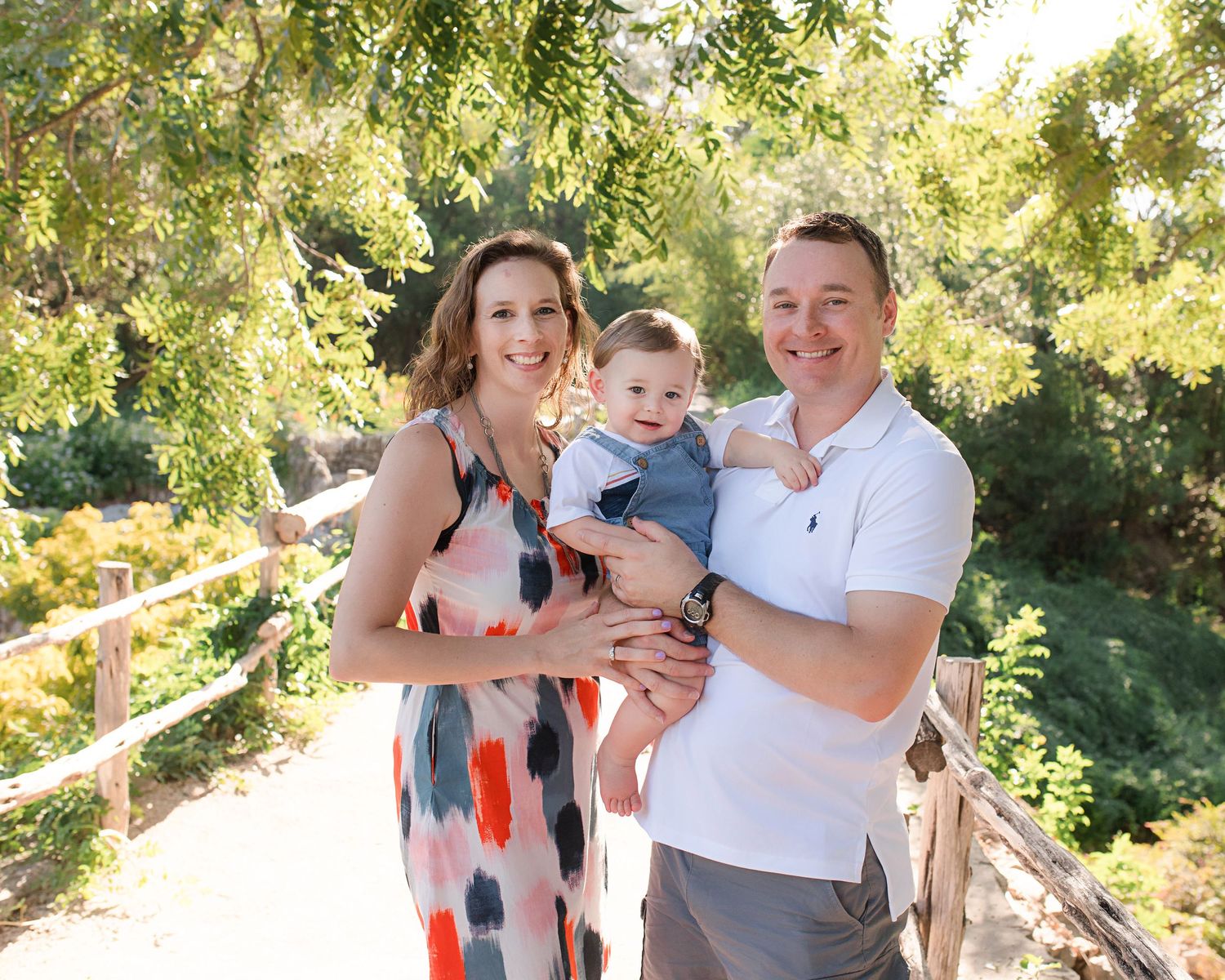 Summer family portrait on wooden bridge path surrounded by green foliage.