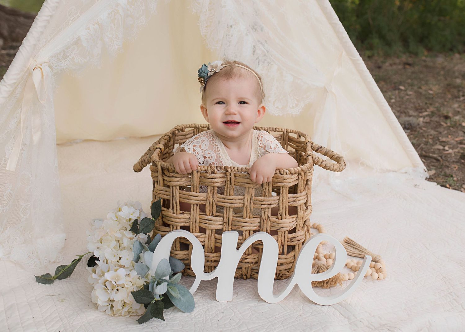 Baby milestone photo in wicker basket with 'one' text and floral decorations.