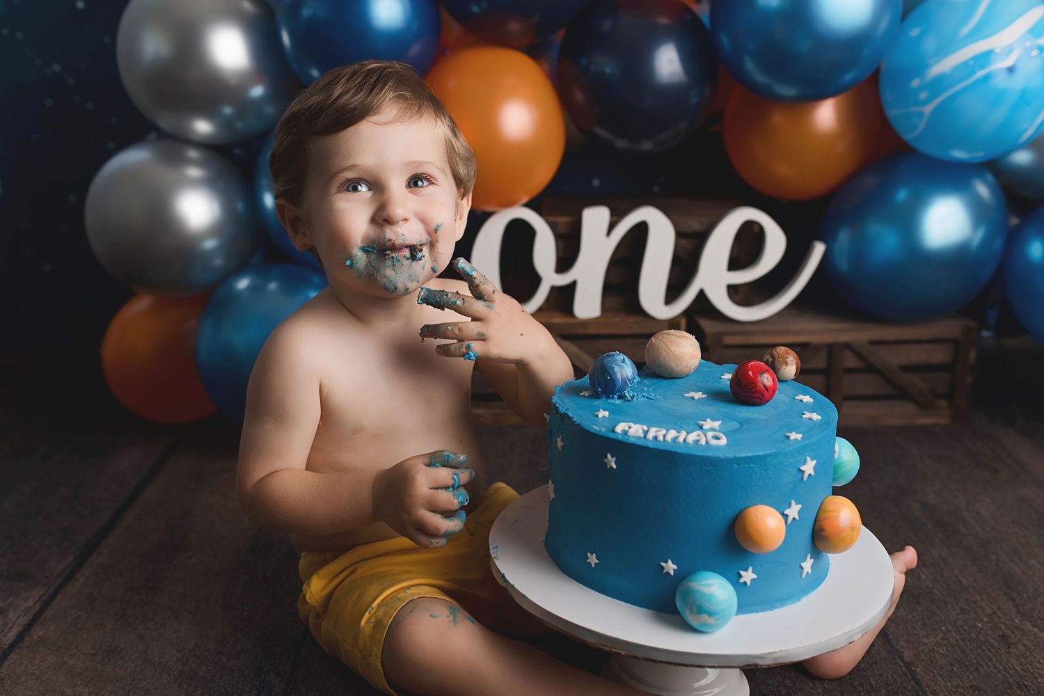 First birthday cake smash session with blue cake and balloon decorations.