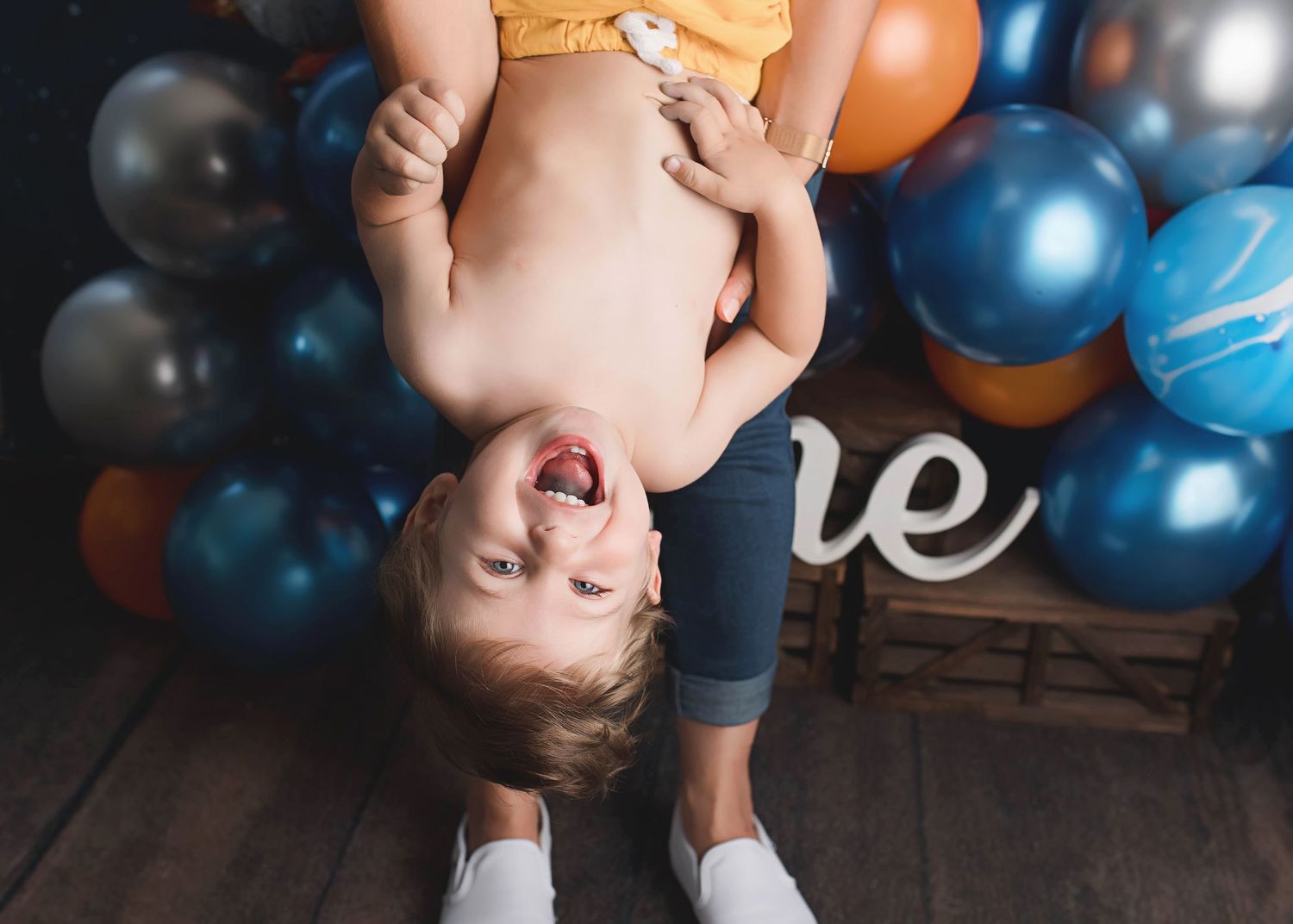 Playful upside down photo with balloons and 'one' sign in background.
