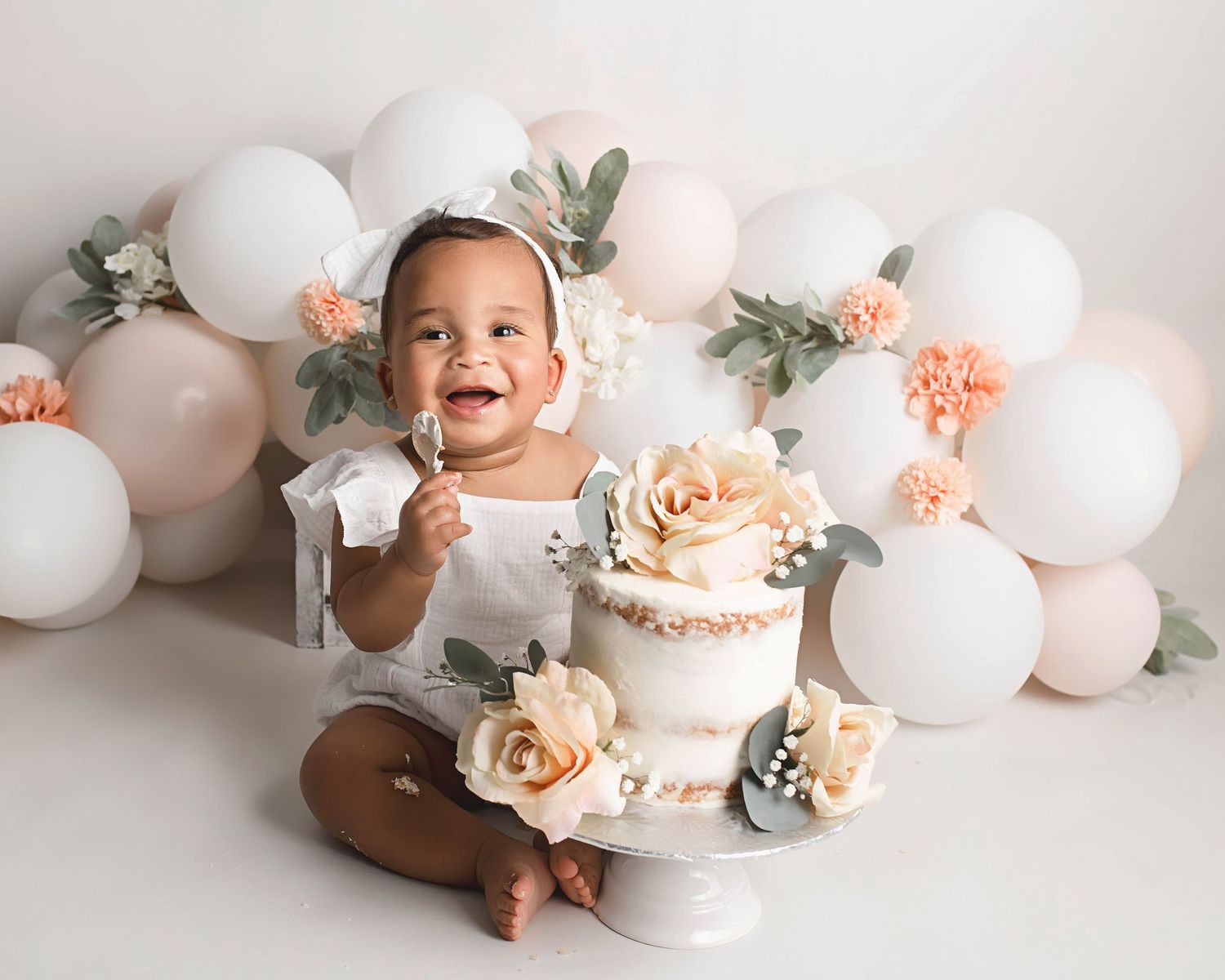 Happy baby celebrating first birthday with elegant floral cake and balloon display.
