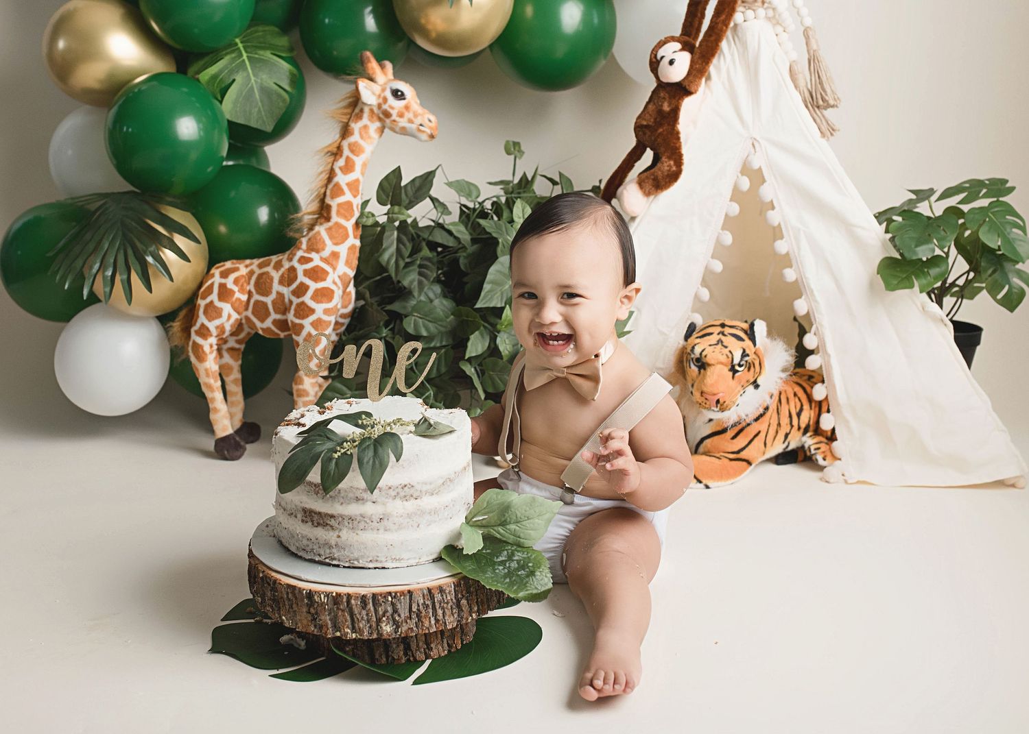 Baby celebrating first birthday with safari themed cake smash and decorations.