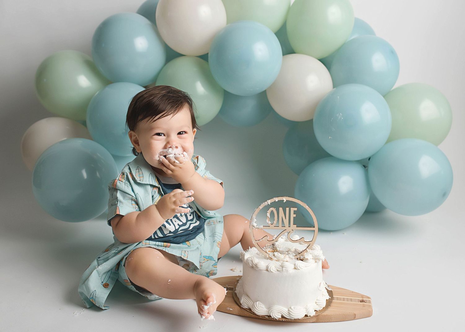 First birthday cake smash photoshoot with blue and white balloon garland backdrop.
